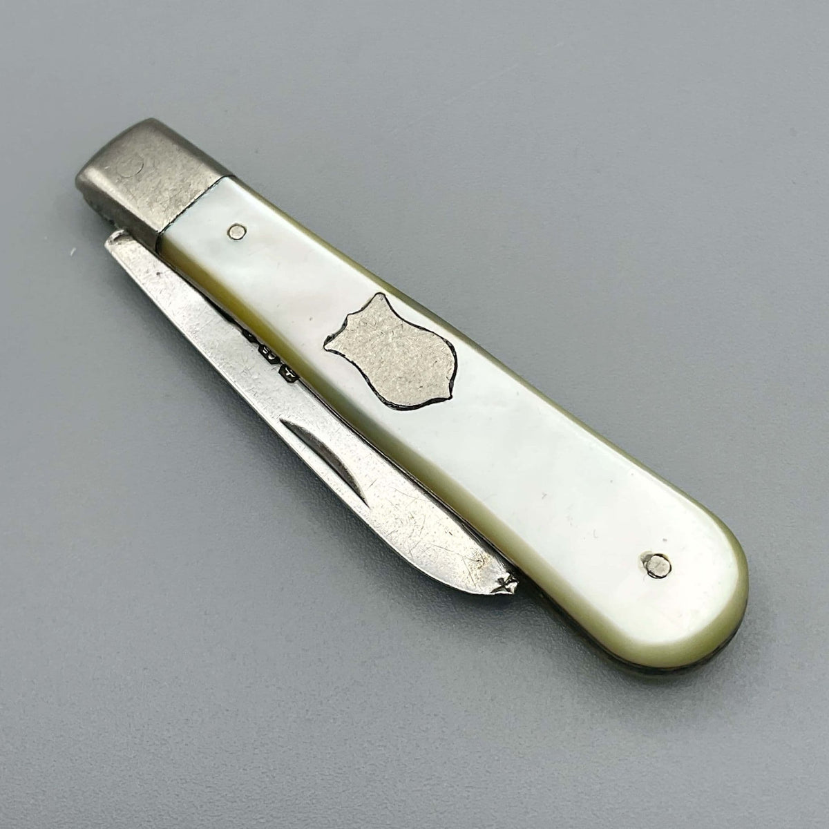 Silver fruit knife with a mother of pearl handle with the blade folded away on a grey background.