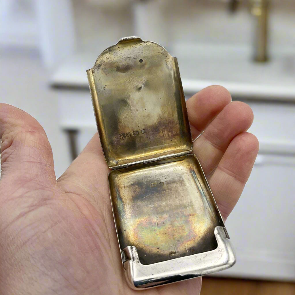 Silver matchbook case with the gilded interior showing held in a hand and marble kitchen background 