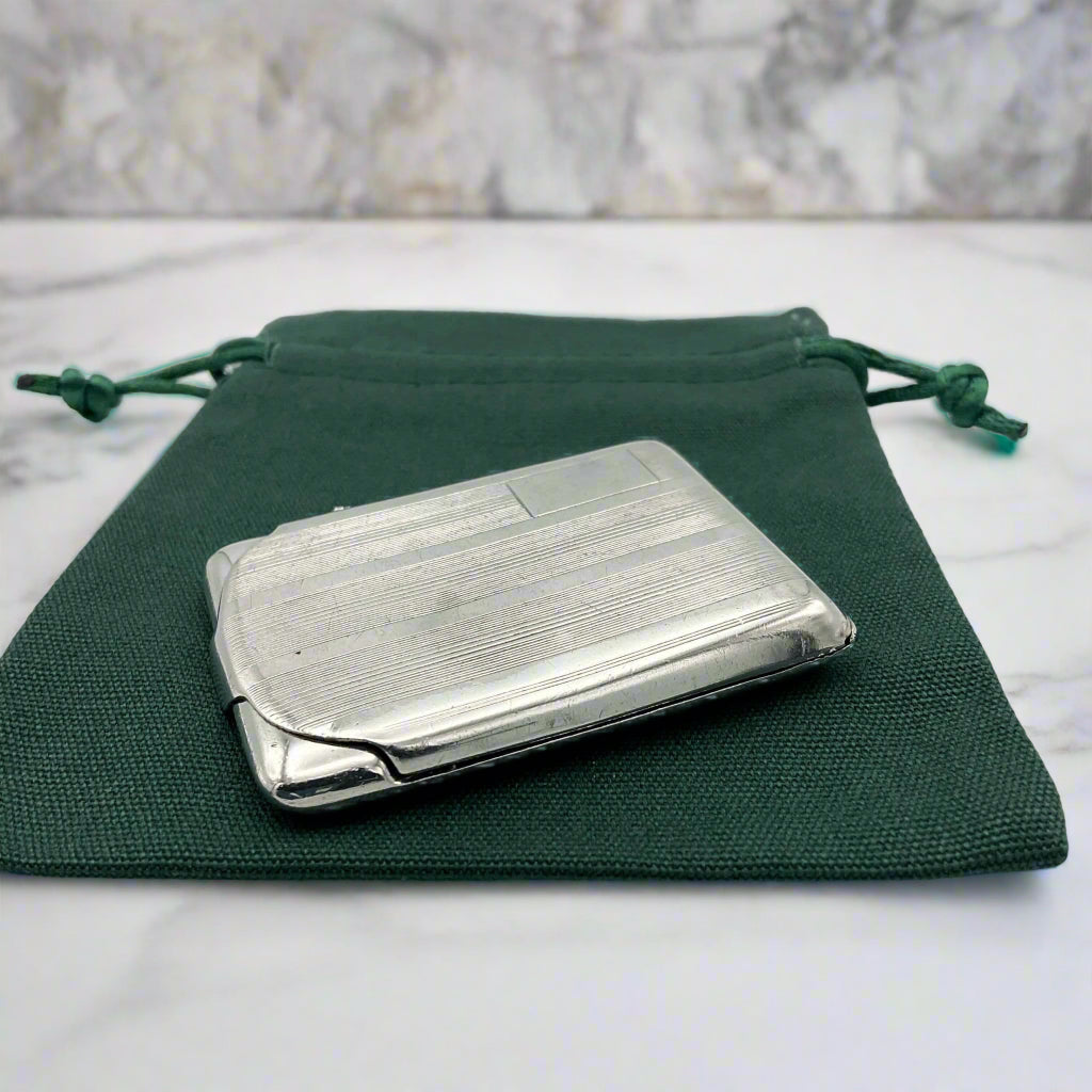 Side view of Silver matchbook case with a lined pattern and blank box for engraving initials in left hand corner on a green gift bag.