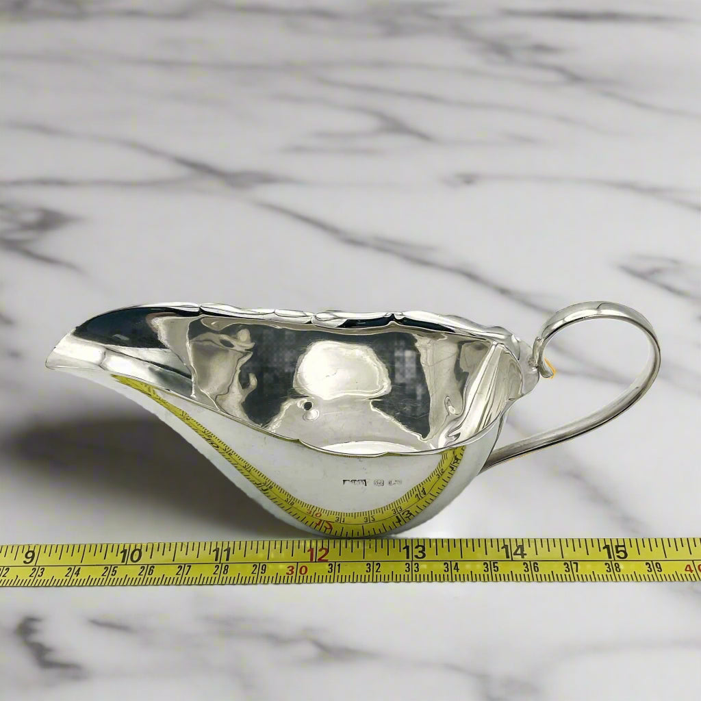 Silver gravy boat next to tape measure showing length as 15.5cm on a marble surface