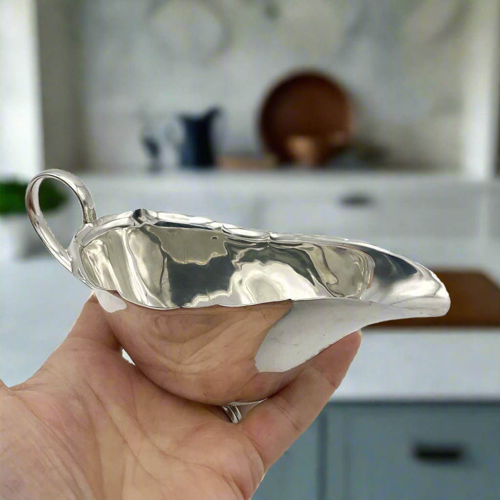 Silver gravy boat held in a hand with a marble kitchen in background