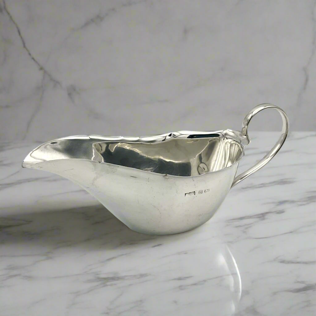 Silver gravy boat with hallmarks on marble background 
