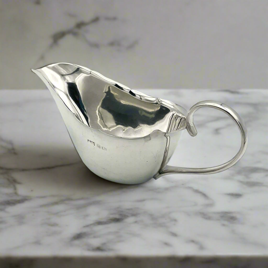 Back of silver gravy boat showing hallmarks and loop handle on a marble worktop