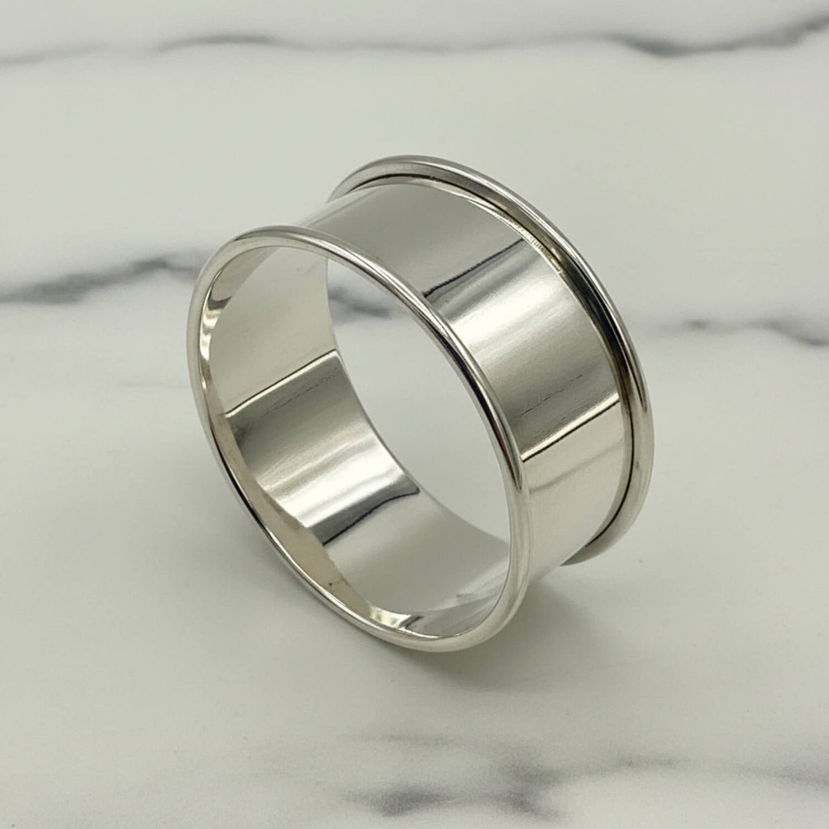 A polished silver napkin ring with a wide, flared band and a smooth, reflective finish, photographed on a light gray background.