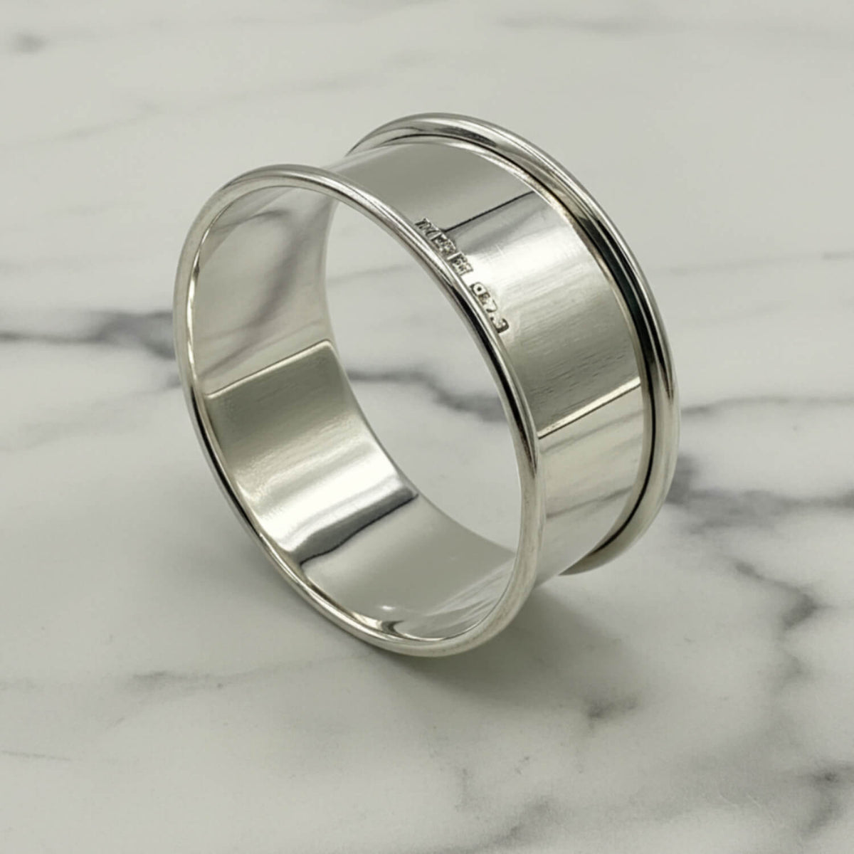 A polished silver napkin ring showing hallmarks on the outside, resting on a white marble surface.