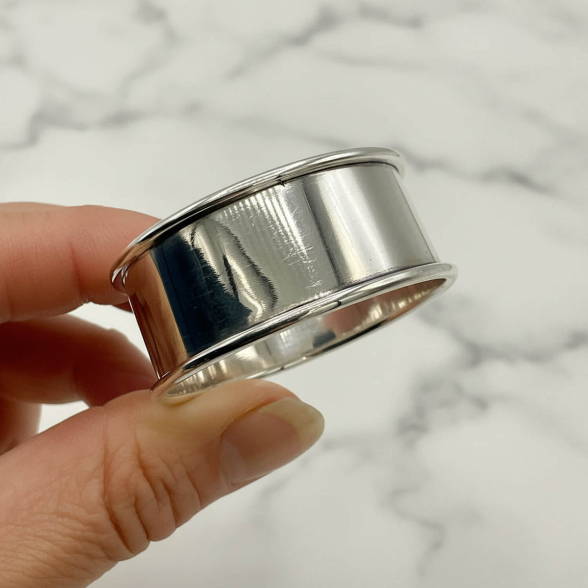 A polished napkin ring being held between fingers against a plain light background.