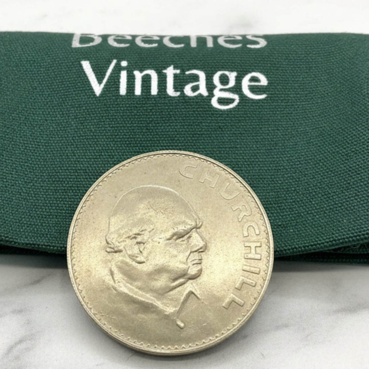 Coin with a portrait on a green fabric background with 'Beeches Vintage' branding.
