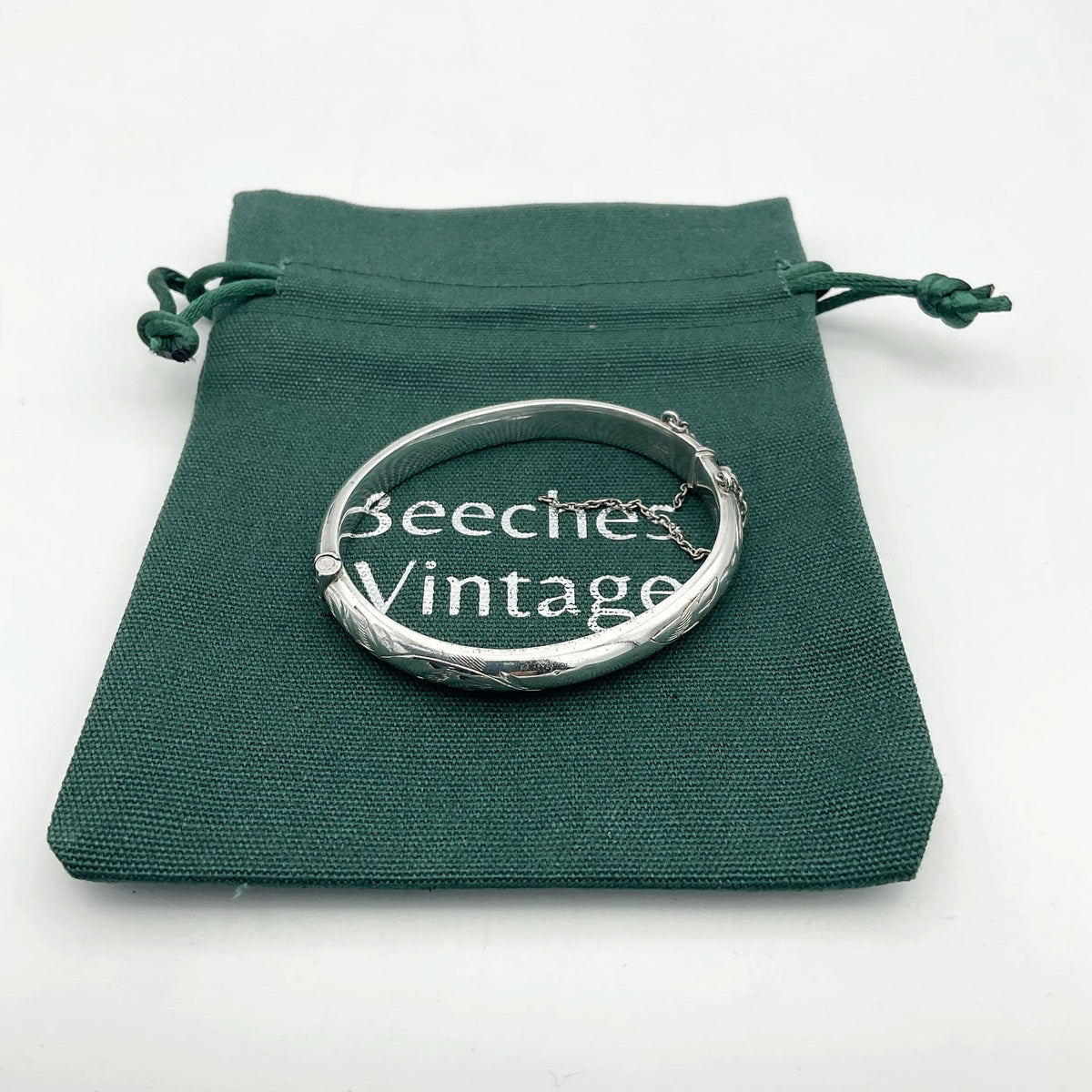 Small silver bracelet with a etched design and chain on a green bag