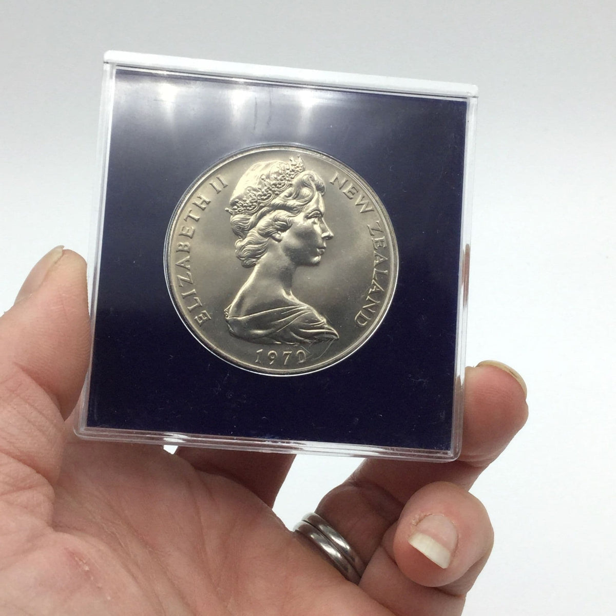 Reverse side of Cook Islands dollar coin with a ship on it in a blue case held in hand