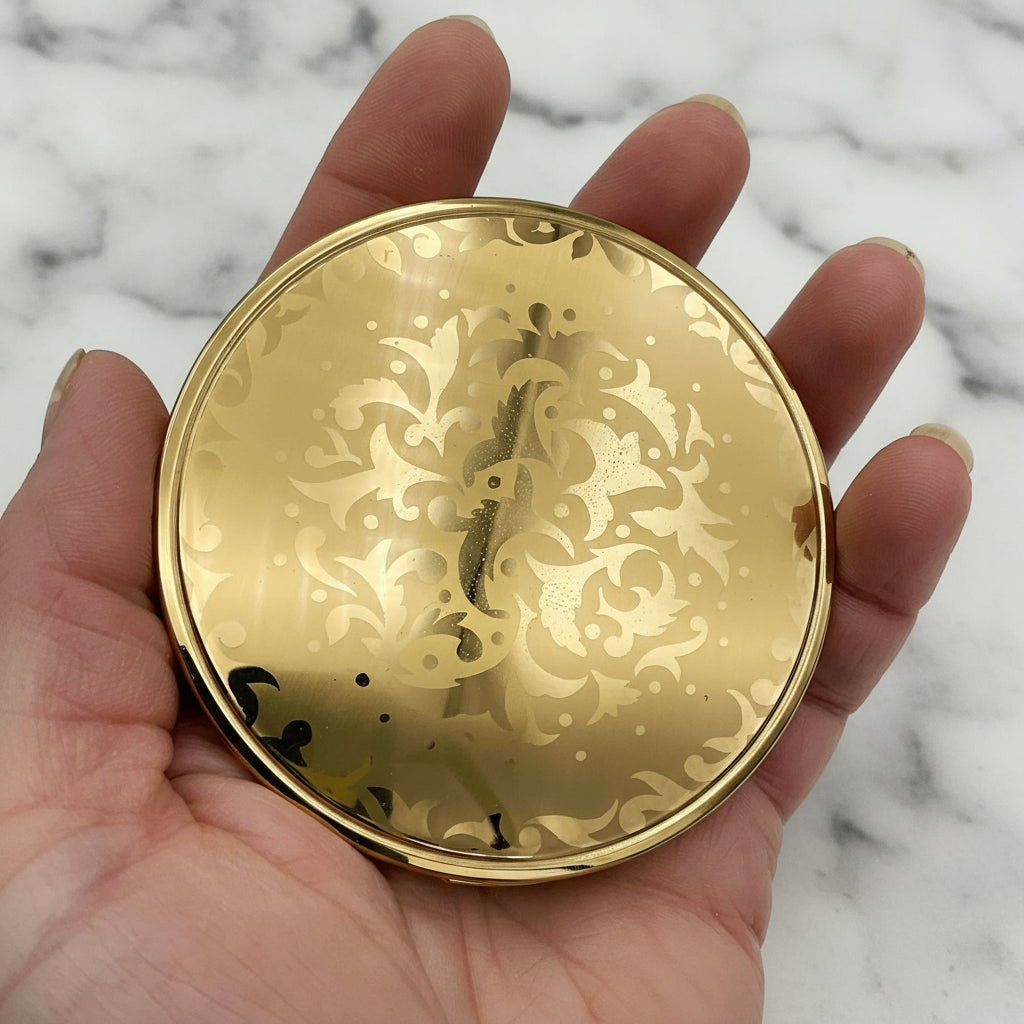 beautiful gold patterned lid of powder compact held in a hand with marble background 