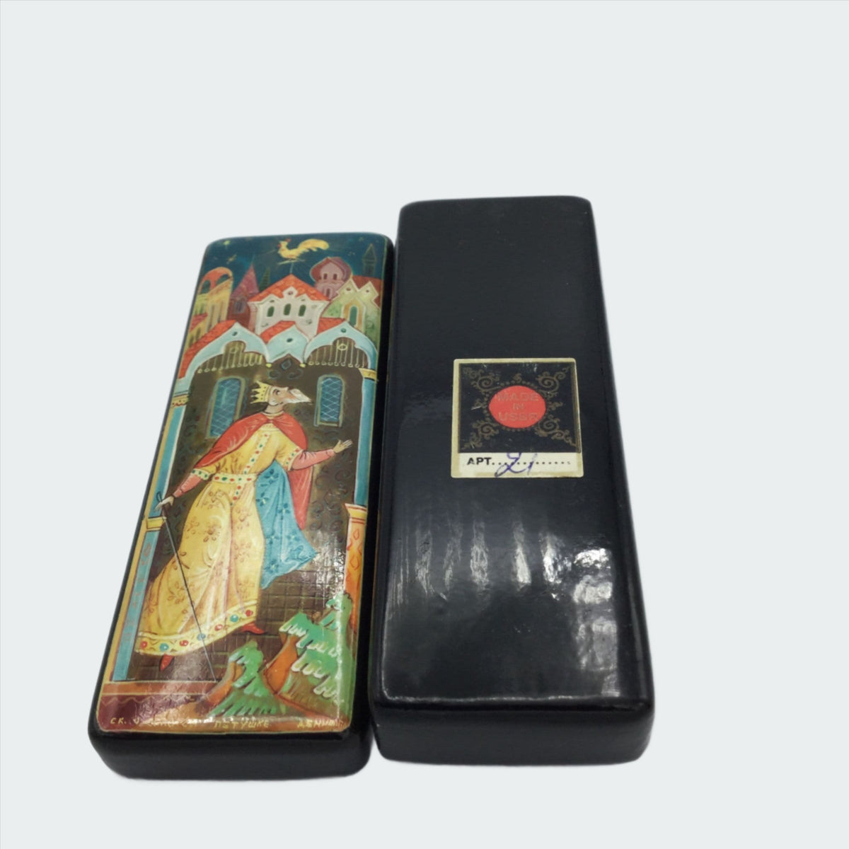 Black handpainted box with a colourful painting of a king looking at a cockerel above him and the base with the Apt 21 sticker on it