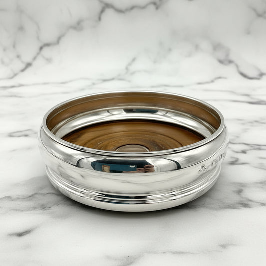 Silver bottle coaster with wooden interior on a marble surface