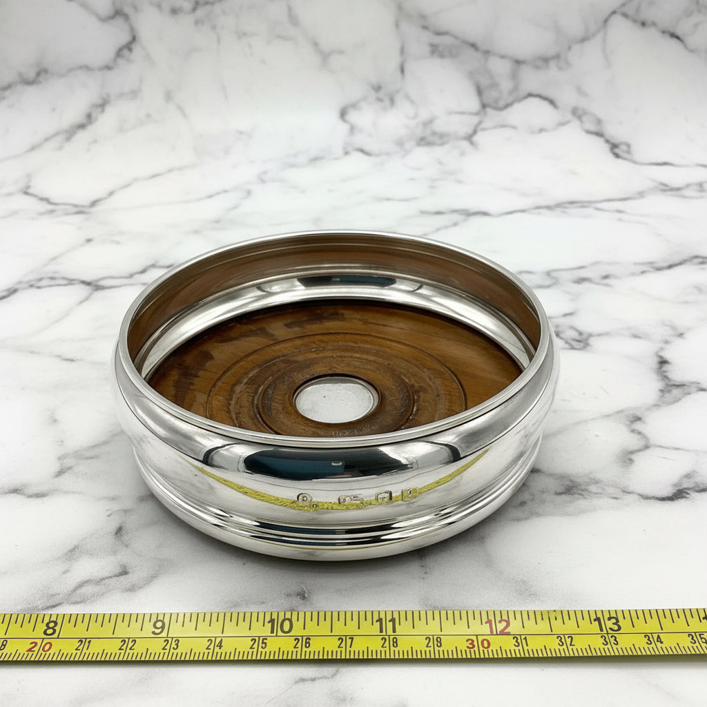Silver and wooden circular bottle coaster on a marble surface with a measuring tape for scale.