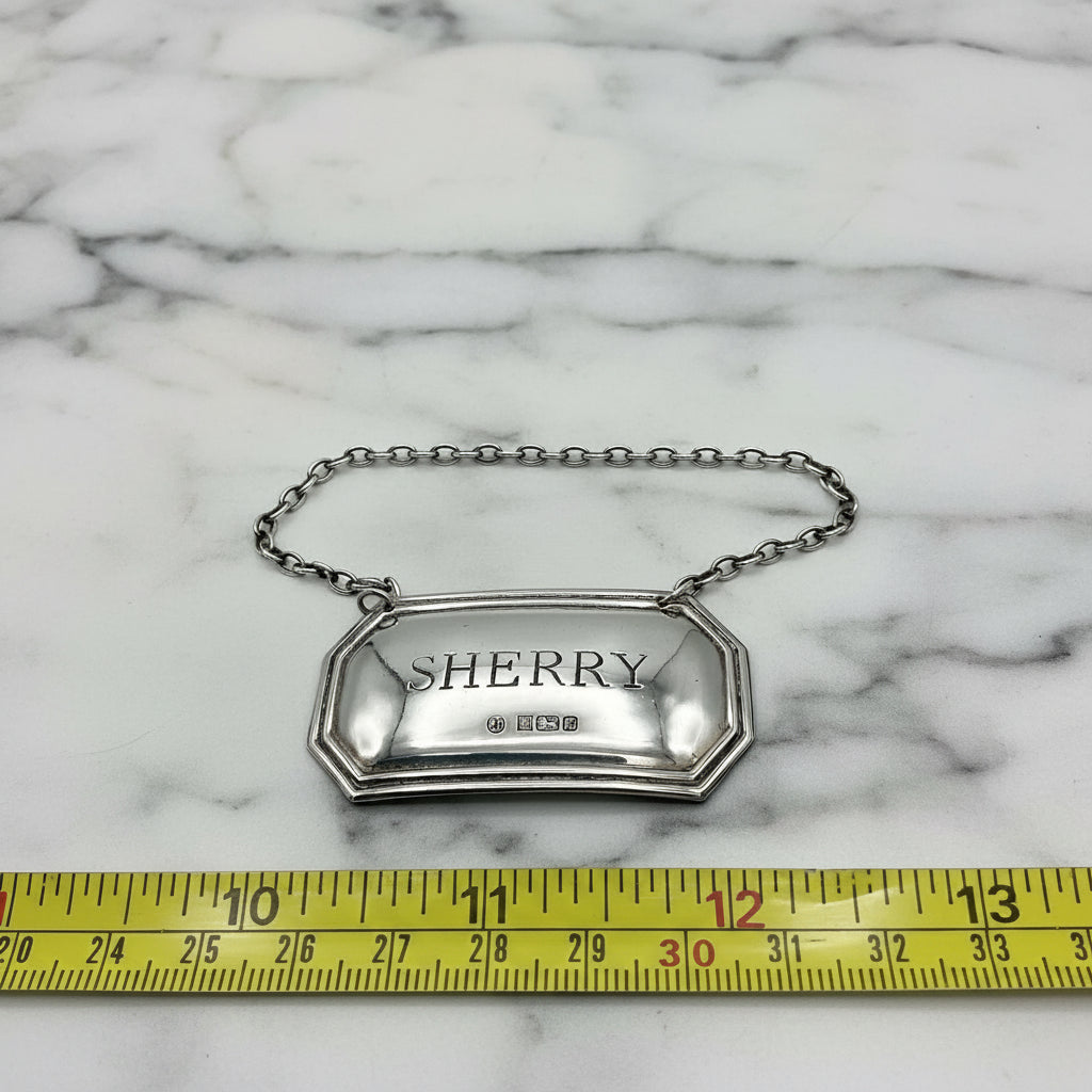 sherry silver decanter label next to a tape measure on a marble background