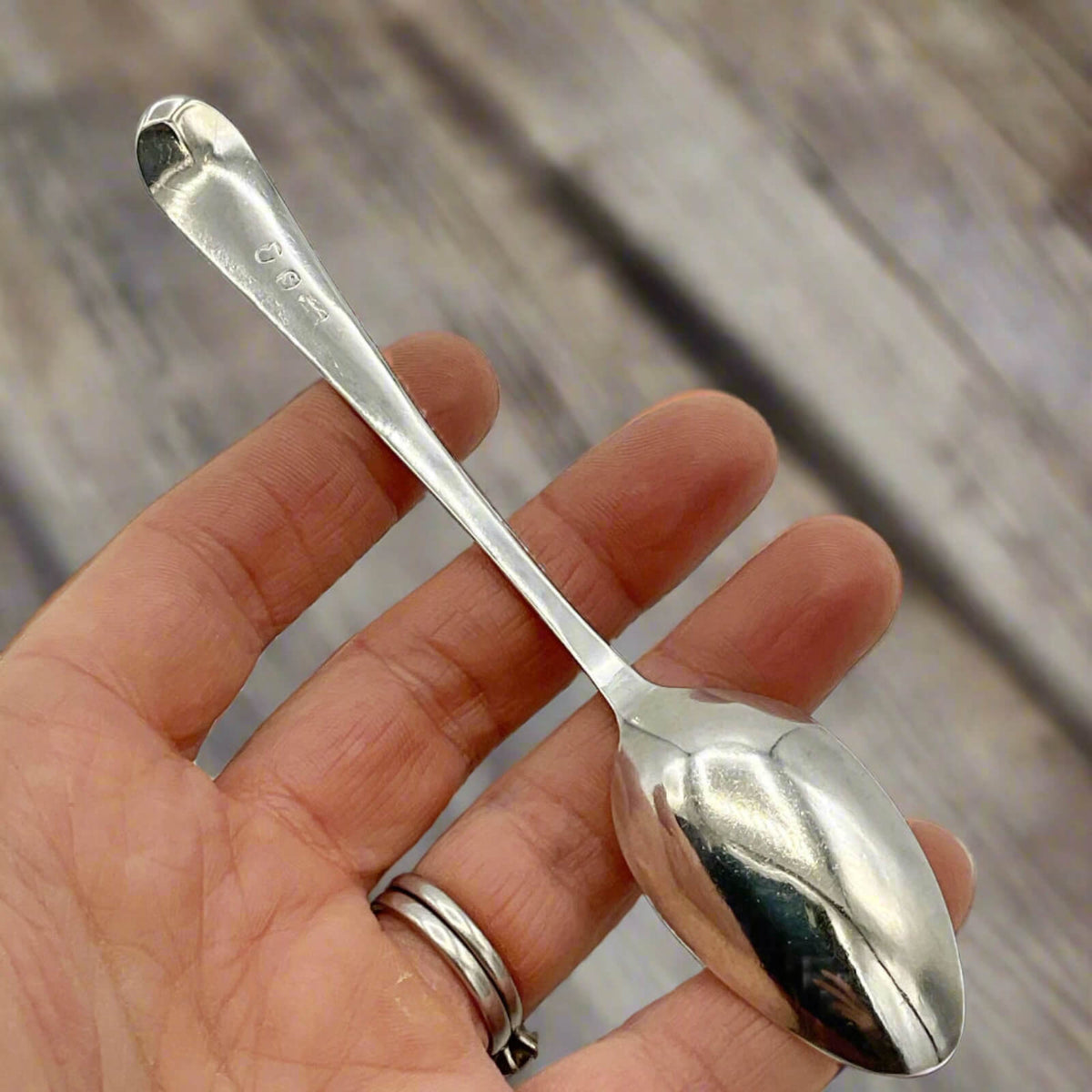 Hand holding a silver spoon with a blurred wooden background