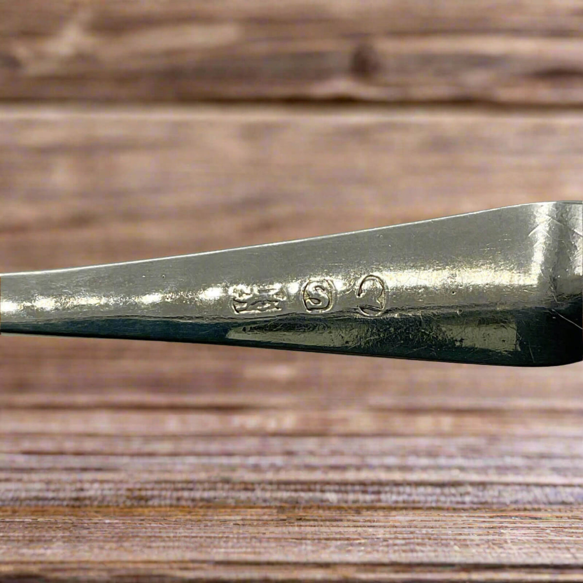 Close-up of a silver spoon handle with engraved hallmarks on a wooden surface