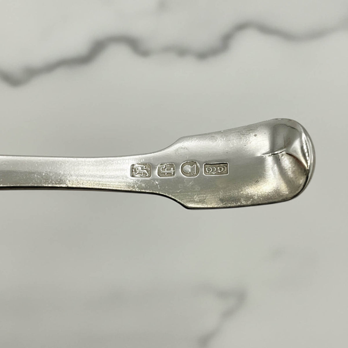 Antique 1800s Silver Tea Caddy Spoon with hallmarks and a marble surface in the background
