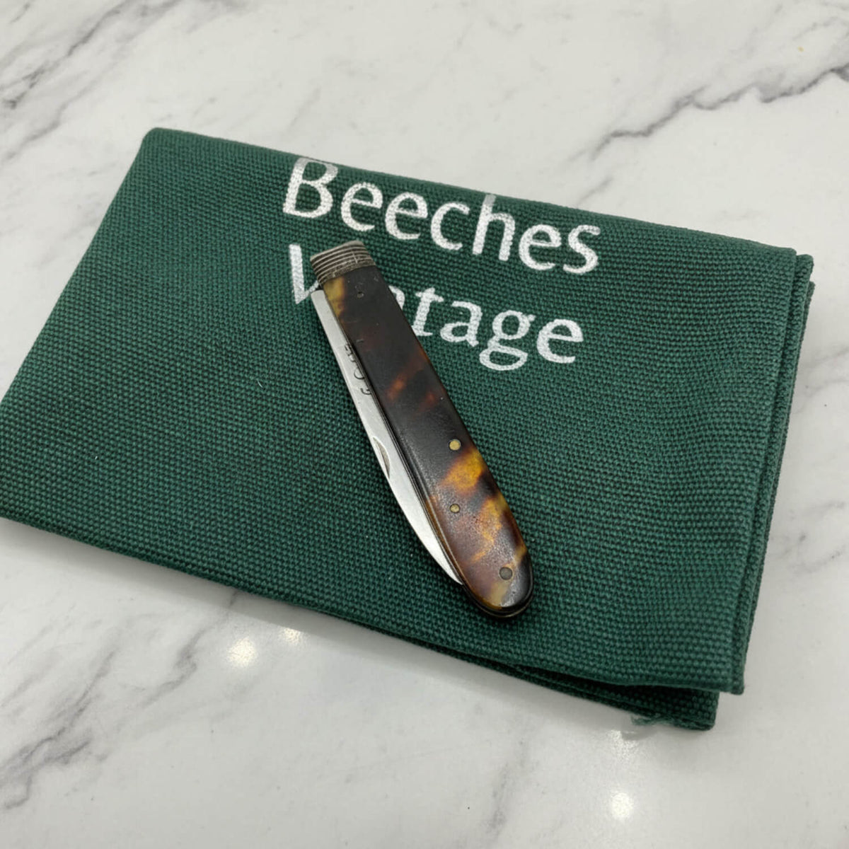 Antique 1819 Sterling Silver Fruit Knife with a tortoiseshell handle and silver blade, resting diagonally on a dark green canvas pouch with 'Beeches Vintage' printed in white.