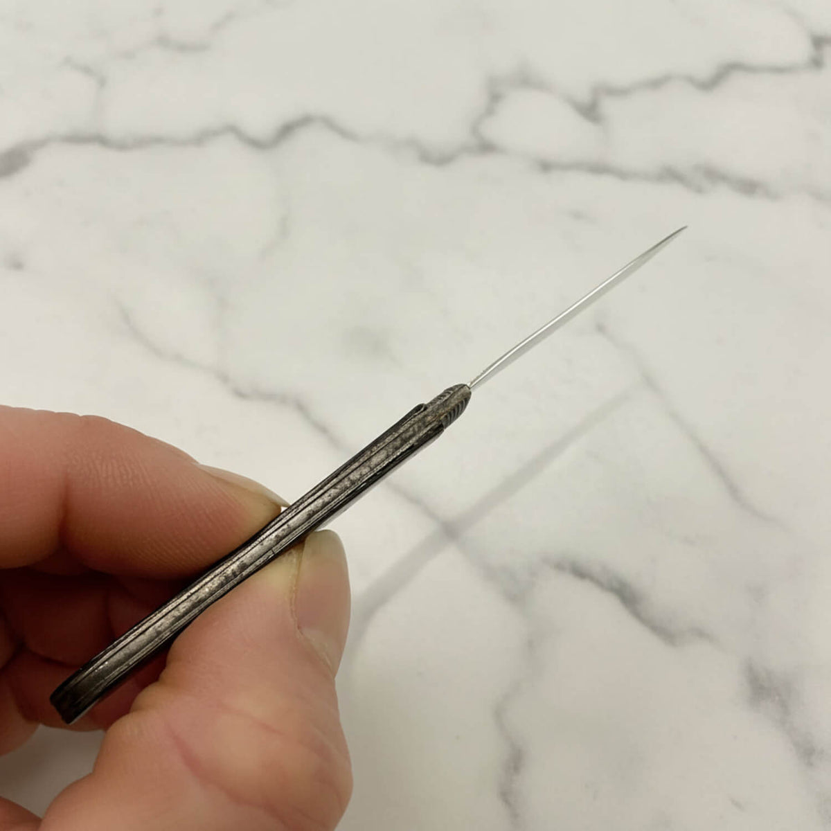 A close-up of a hand holding a fruit knife against a plain off-white background.