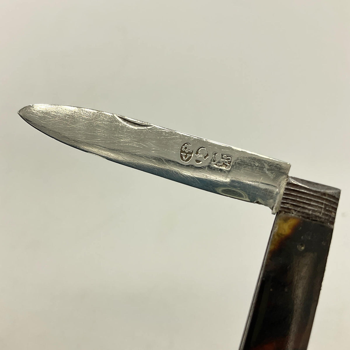 Close-up of a Antique 1819 Sterling Silver Fruit Knife showing hallmarks and a dark brown faux tortoiseshell handle, set against a plain light gray background.