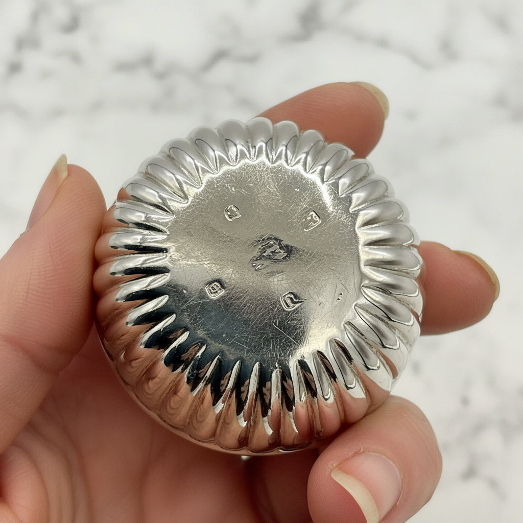 Base of Glided silver Victorian salt held in a hand showing the hallmarks with a white background 