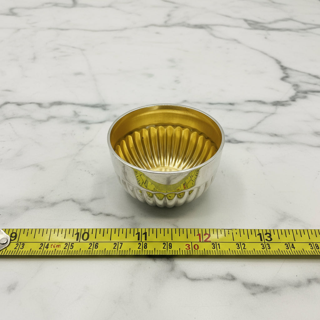 Glided silver Victorian salt next to a tape measure showing the  diameter as 2.5cm on a white background 