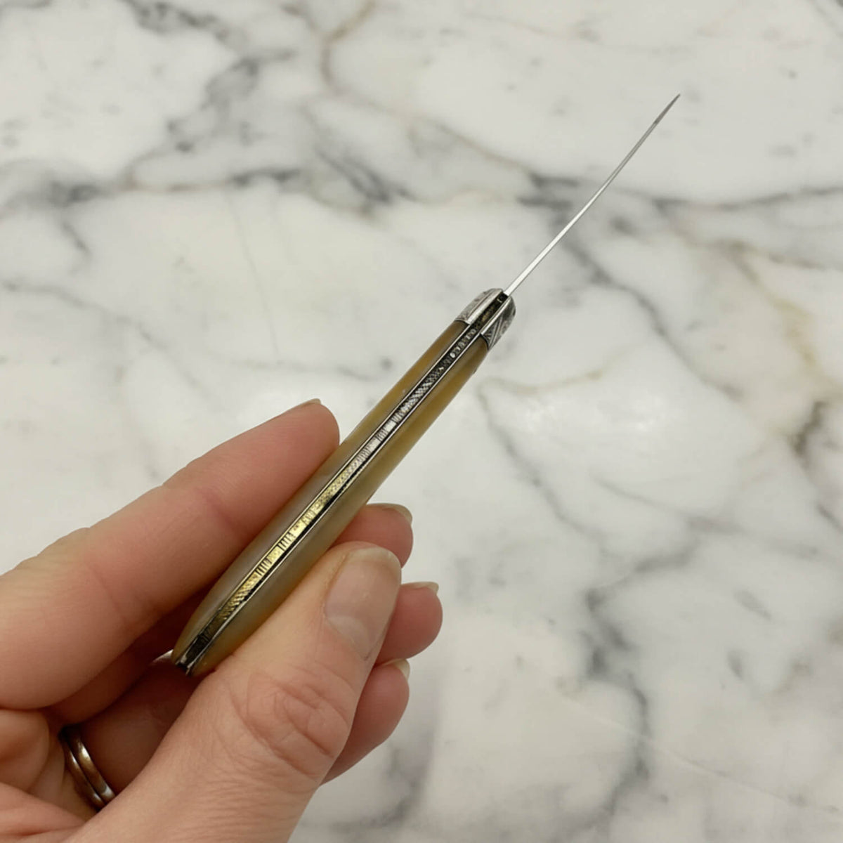 Hand holding a fruit knife showingthe back on a marble background