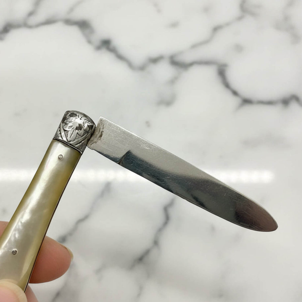Folding knife with decorative handle held against a marble background