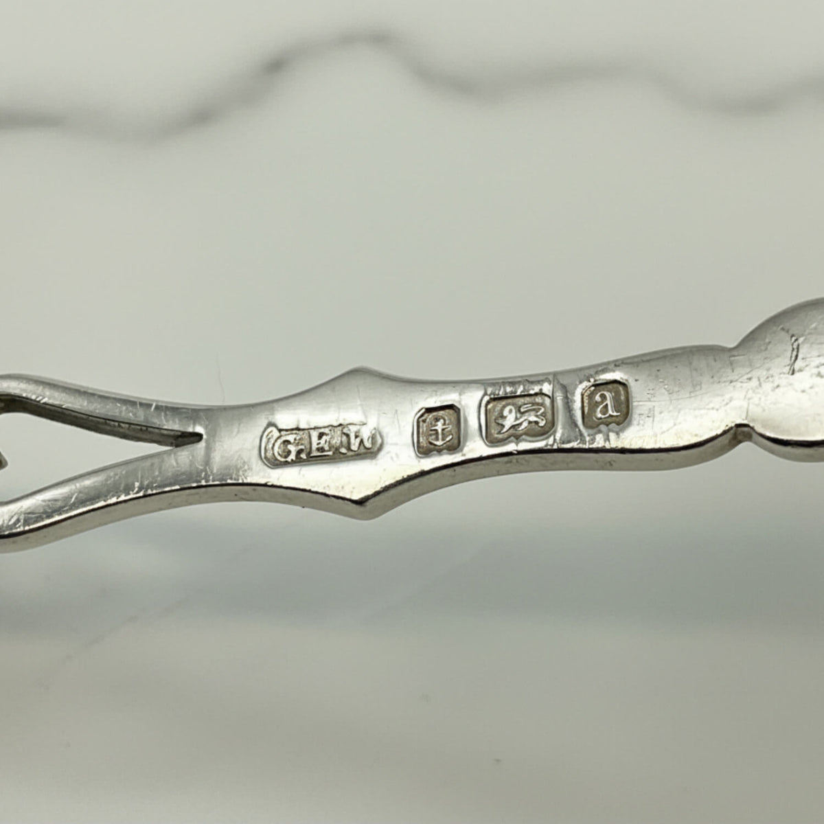 Close-up of a spoon handle showing engraved hallmarks, photographed on a light gray background.