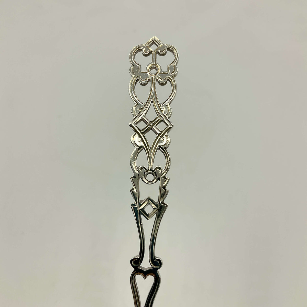An ornate silver sifter spoon handle shown against a plain light gray background.