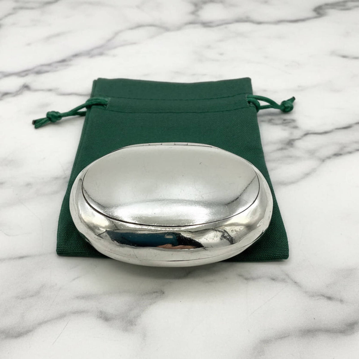 Silver box on a green drawstring pouch with a marble background
