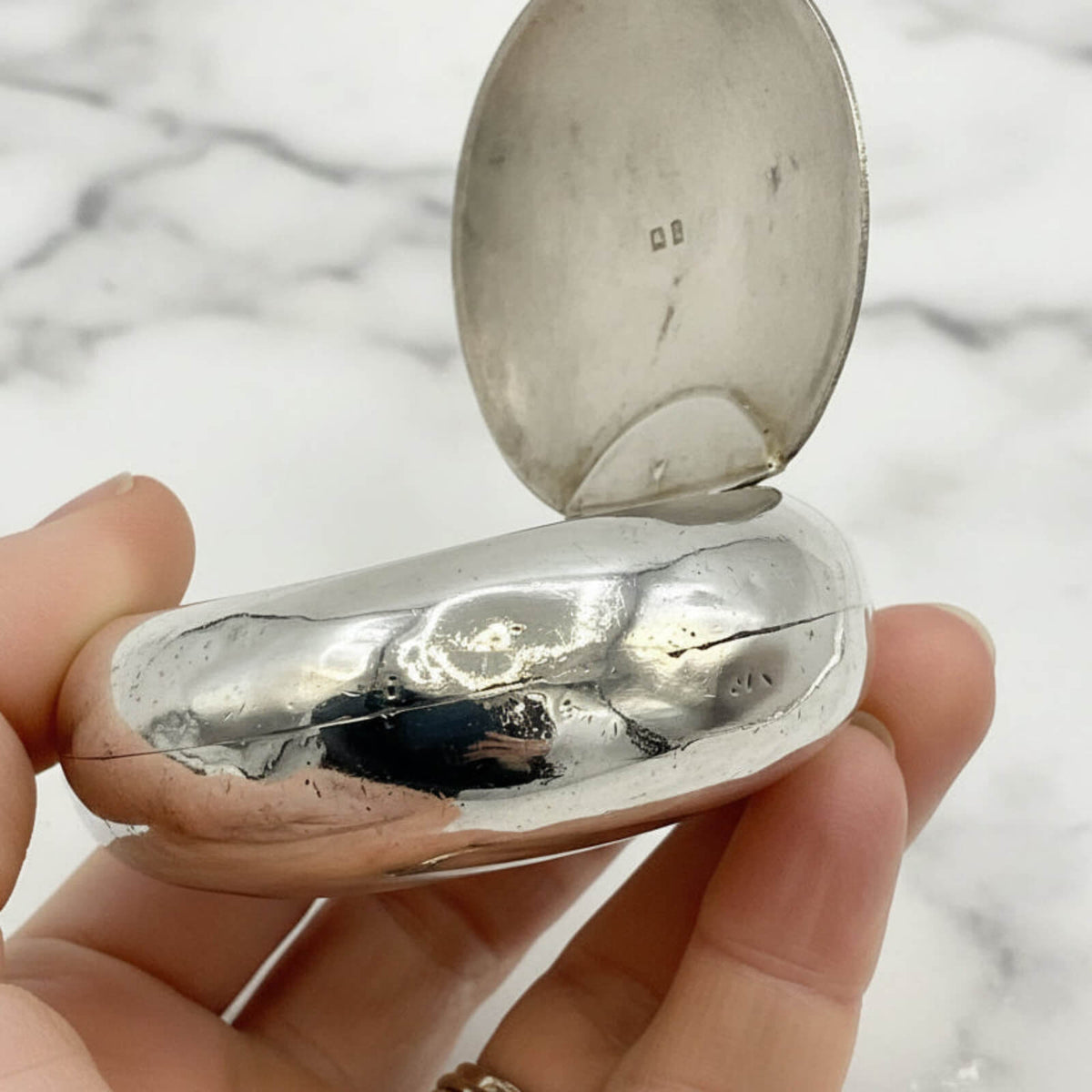 Silver box held in a hand with a marble background