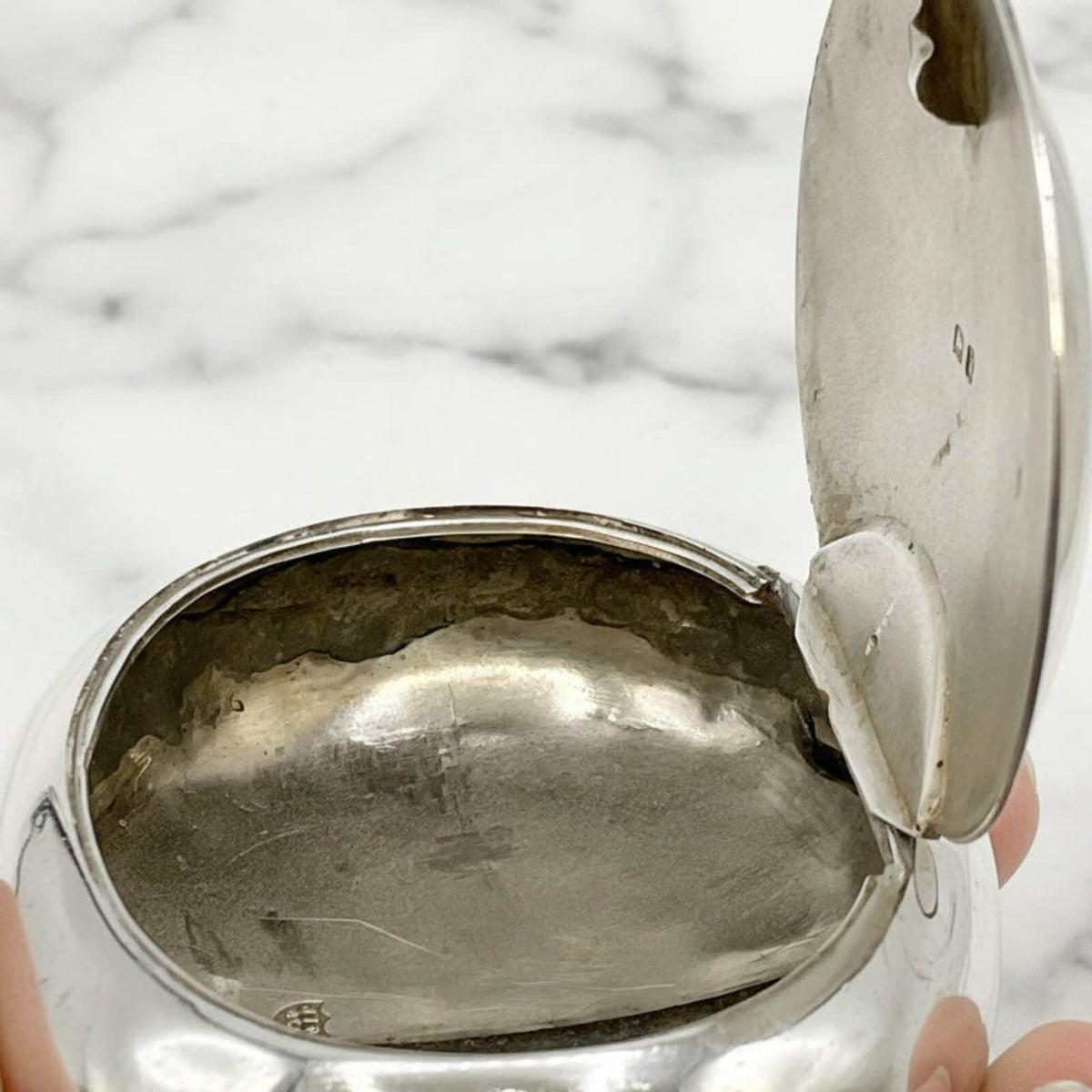 Silver box with a lid held by hands on a marble surface