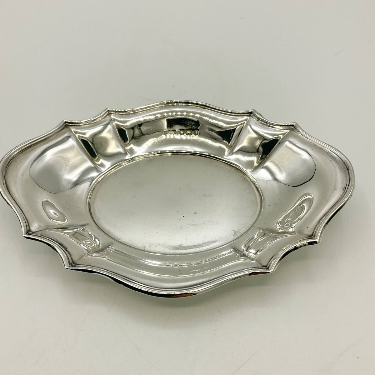 Antique sterling silver serving platter with a scalloped edge and a central oval depression, featuring an engraved hallmark on the inner rim, set against a plain light background.