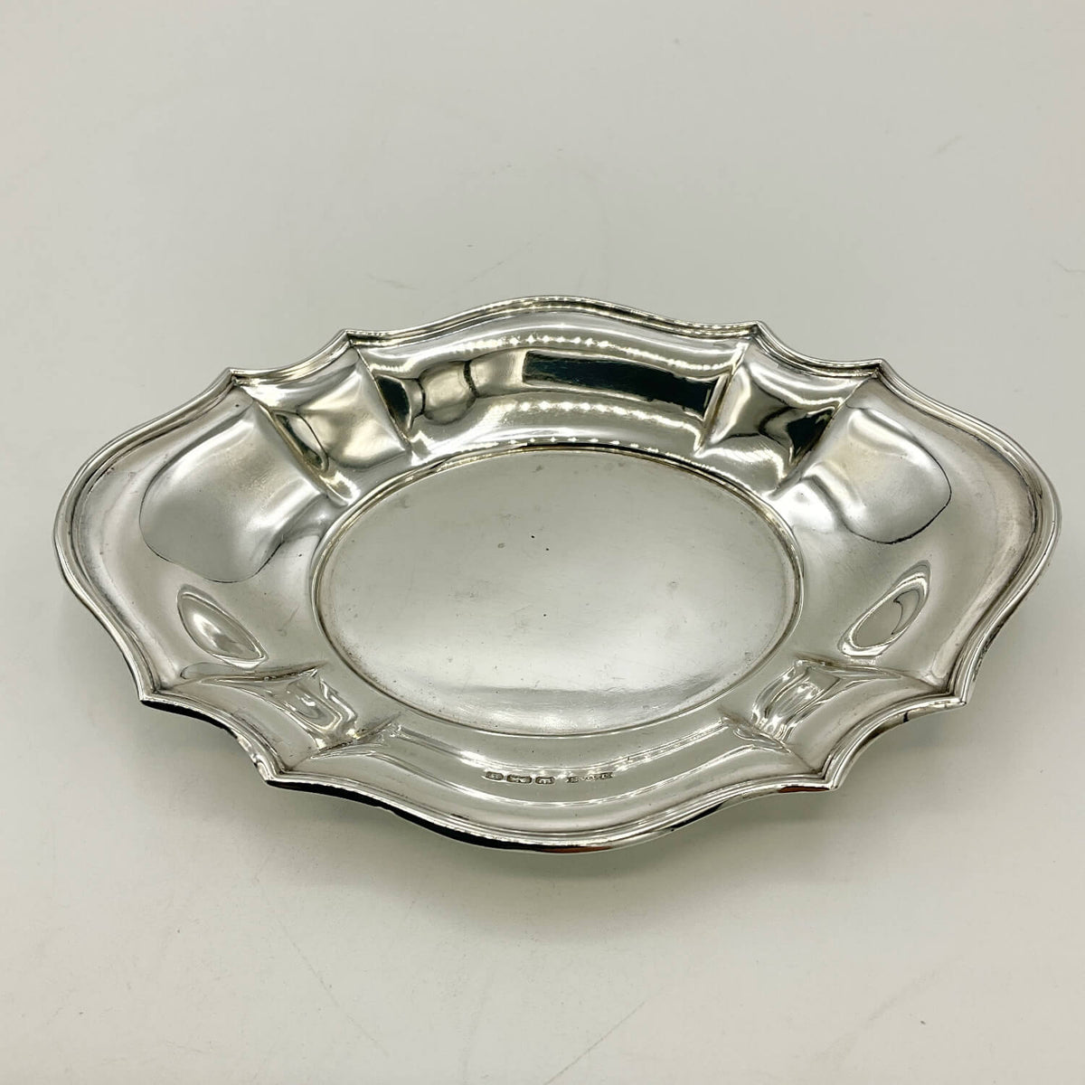 A vintage silver oval pin tray with a scalloped rim and decorative handles, shown on a plain light background.
