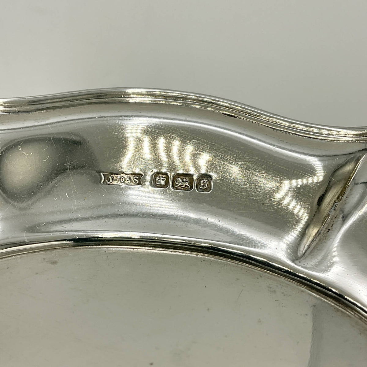 Close-up of the inner edge of a polished silver serving tray or plate, showing stamped hallmarks on the reflective metal surface.