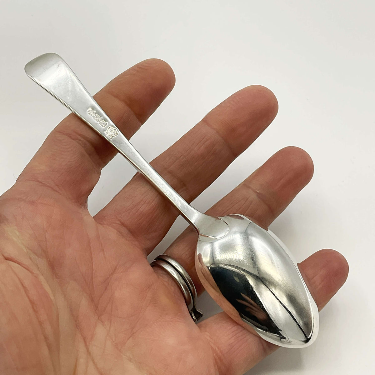 Back of antique silver teaspoon held in a hand with a white background 