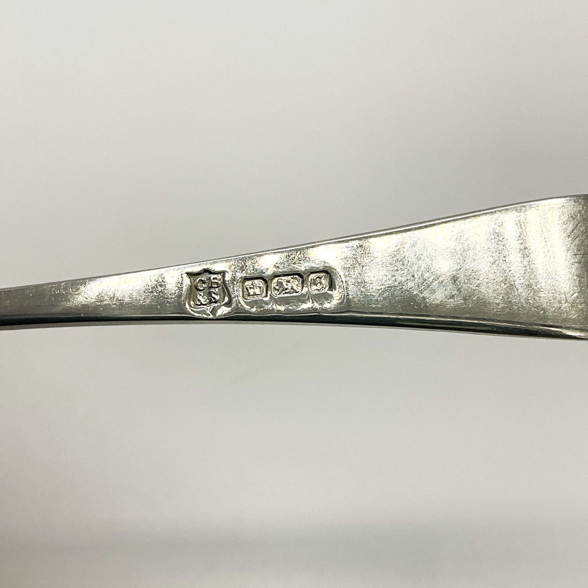 Back of Antique silver teaspoon handle showing the maker’s mark and hallmarks with a white background 