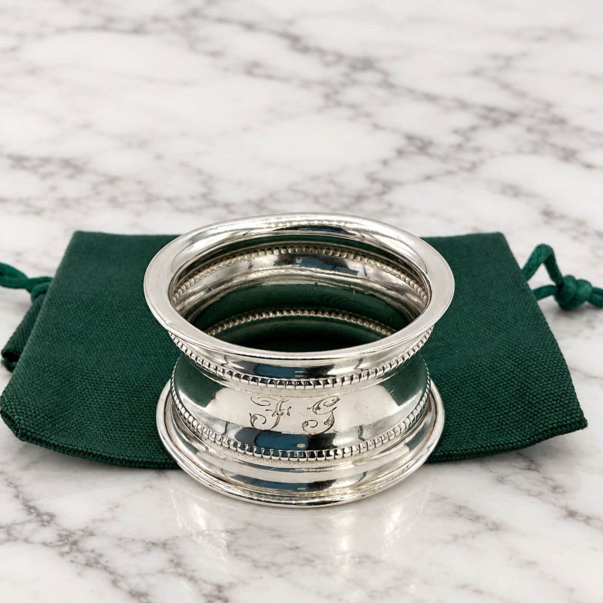 Antique 1912 Sterling Silver Napkin Ring on a green bag on a marble surface