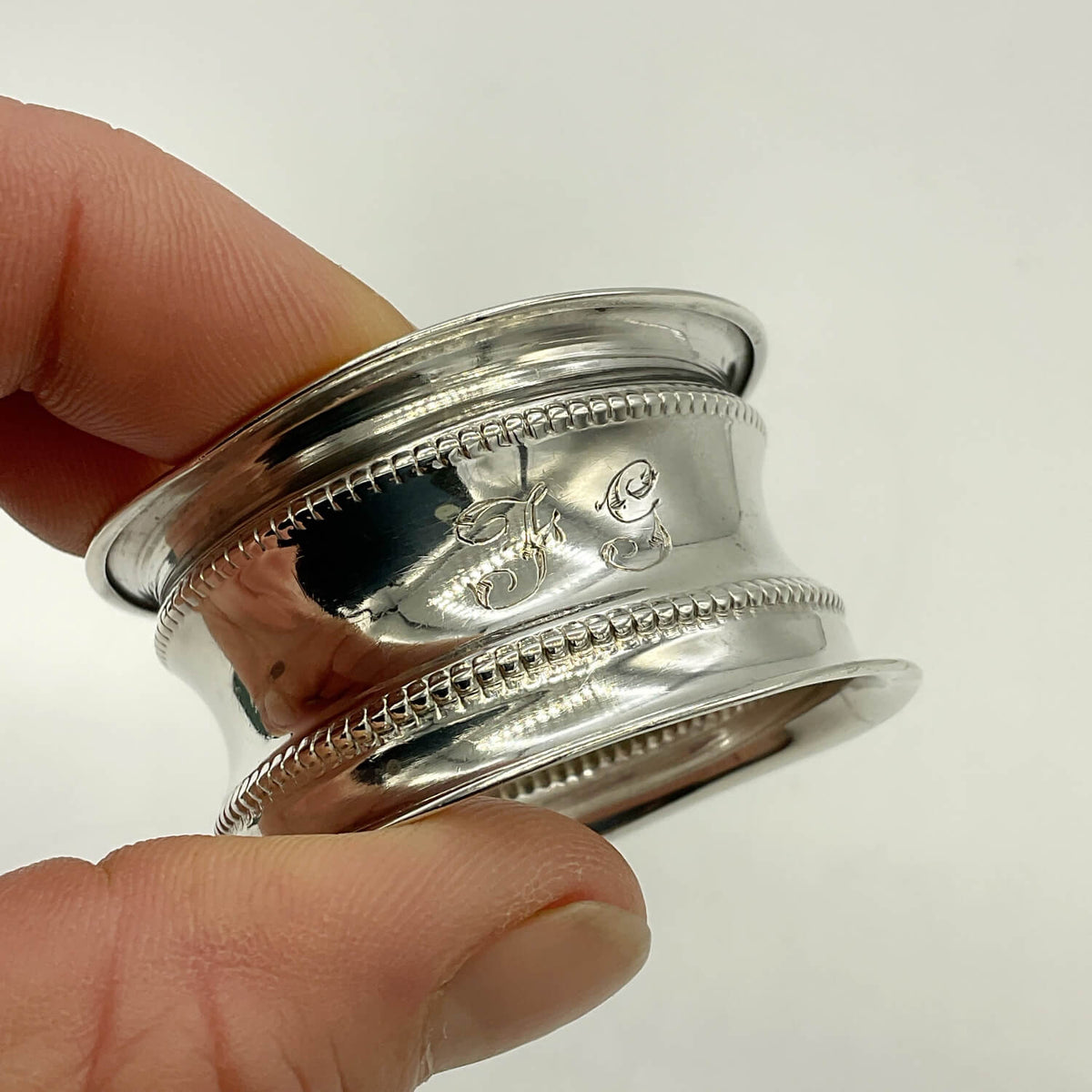 A close-up of a hand holding a polished silver ring with engraved details and a beaded border, set against a plain white background.