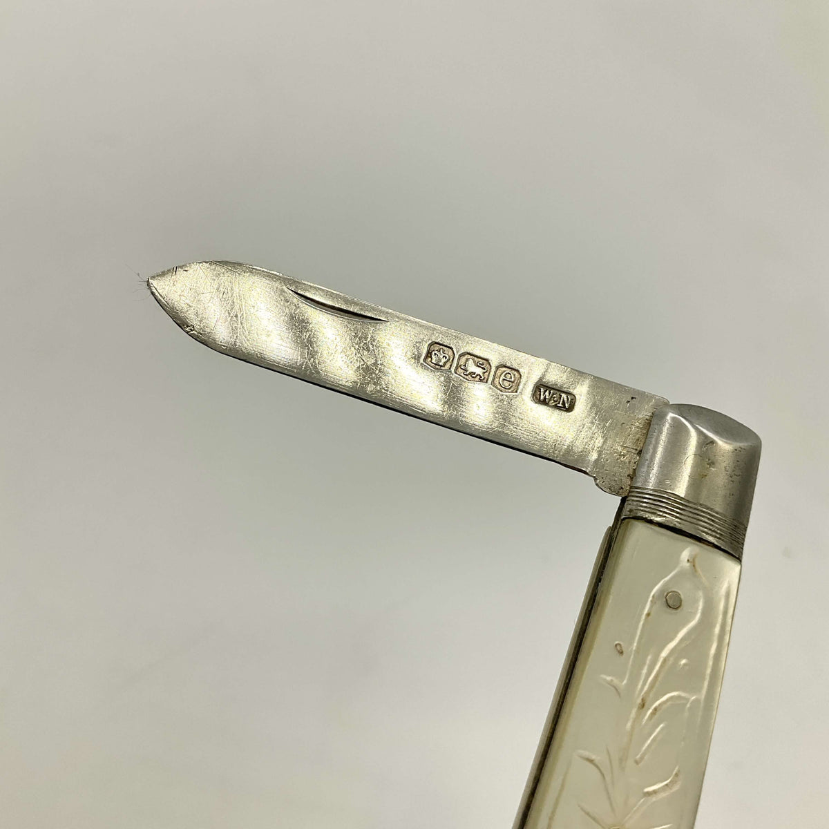 Close-up of a silver fruit knife with engraved handle on a gray background