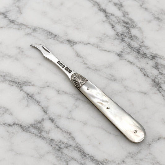 Antique sterling silver toothpick with a mother-of-pearl handle, displayed diagonally on a white and gray marble surface.