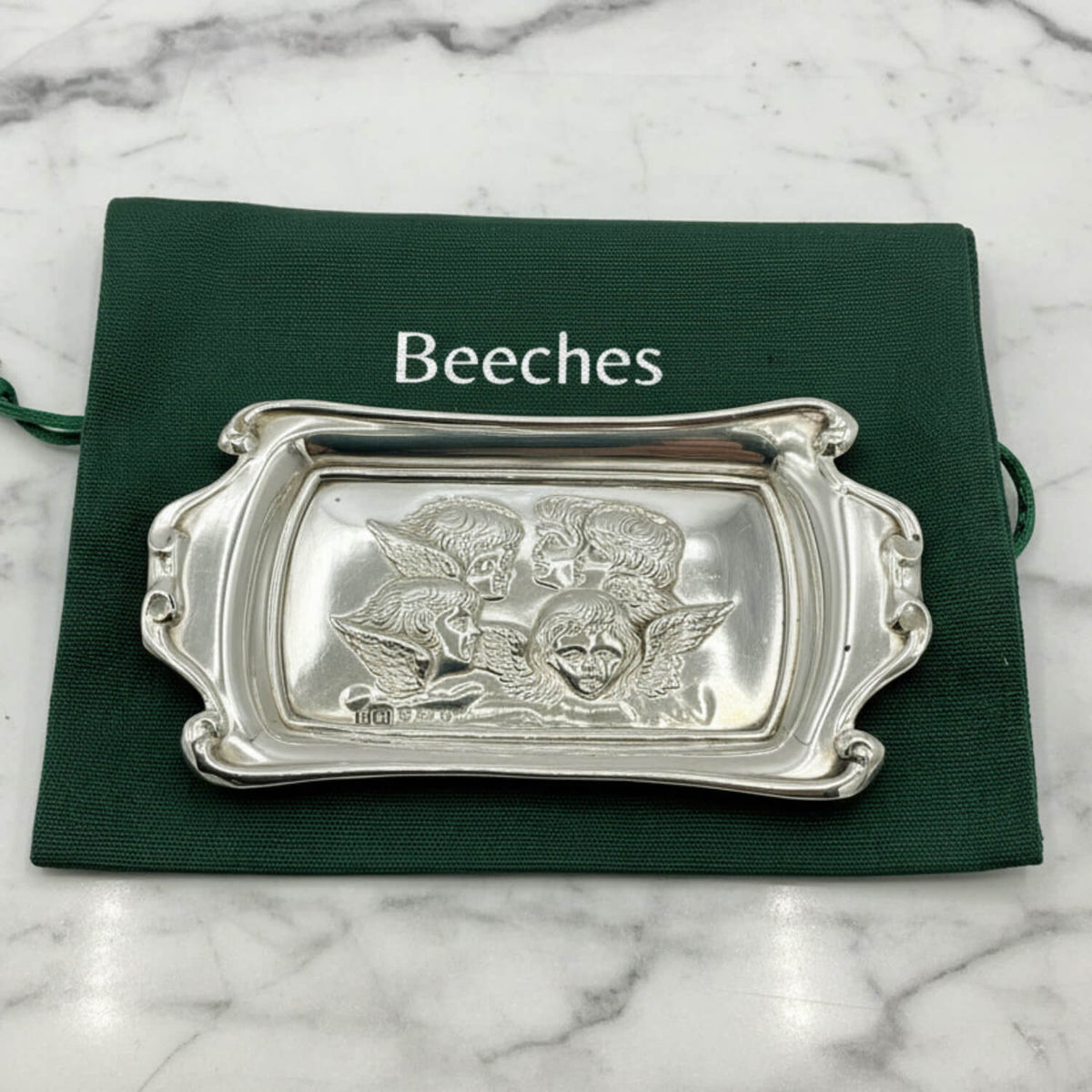 Silver decorative tray with intricate designs on a green cloth labeled 'Beeches Vintage' on a marble background.