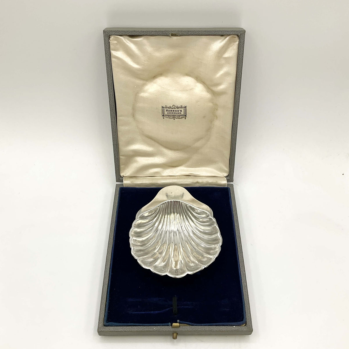 Silver shell-shaped dish in a box with a visible brand name on a white background