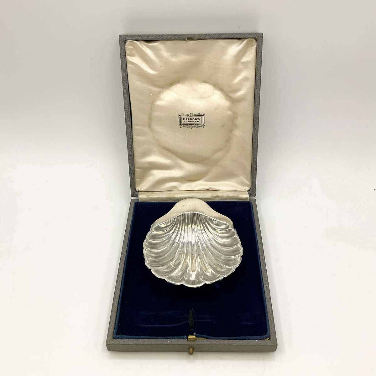 Silver shell-shaped dish in a box with a visible brand name on a white background