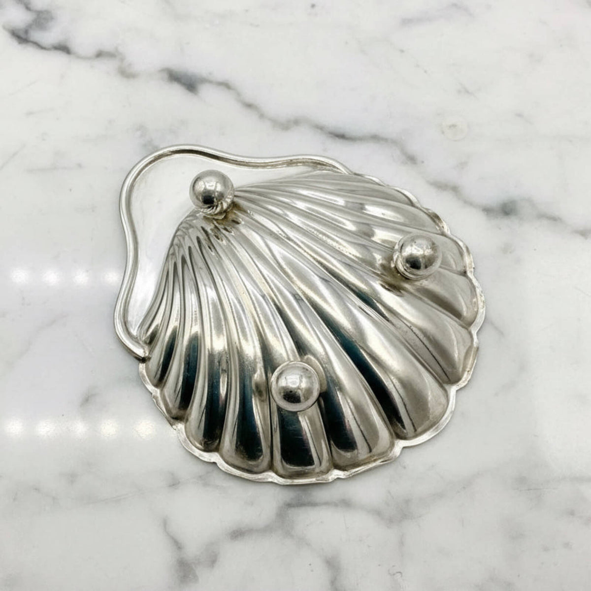 Silver shell-shaped dish with feet on a marble background
