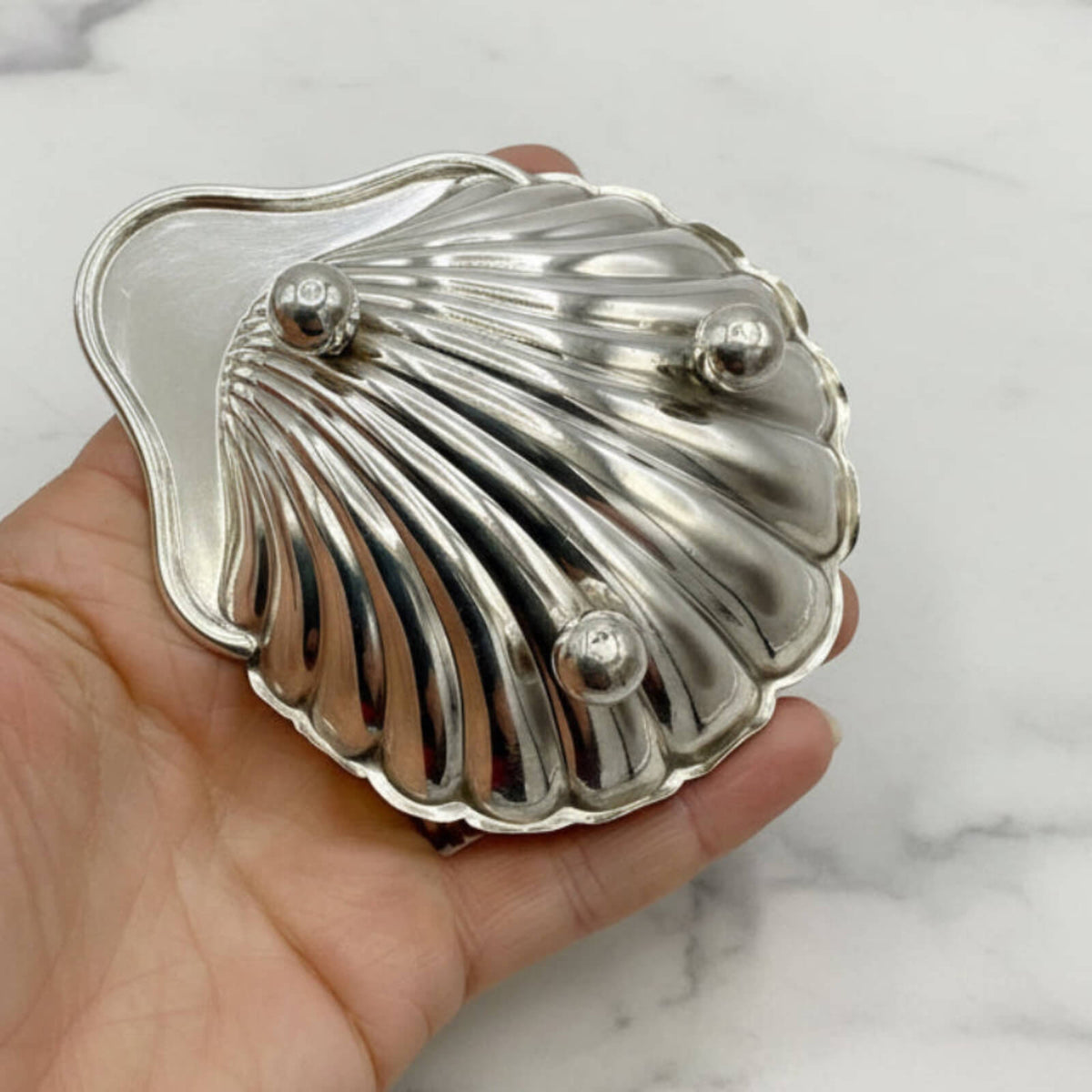 Silver shell-shaped dish held in a hand against a marble background