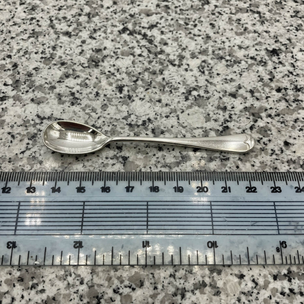 Silver spoon next to a ruler on a speckled surface