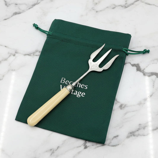 Silver fork with beige handle on a green drawstring bag labeled 'Beeches Vintage' on a marble surface.