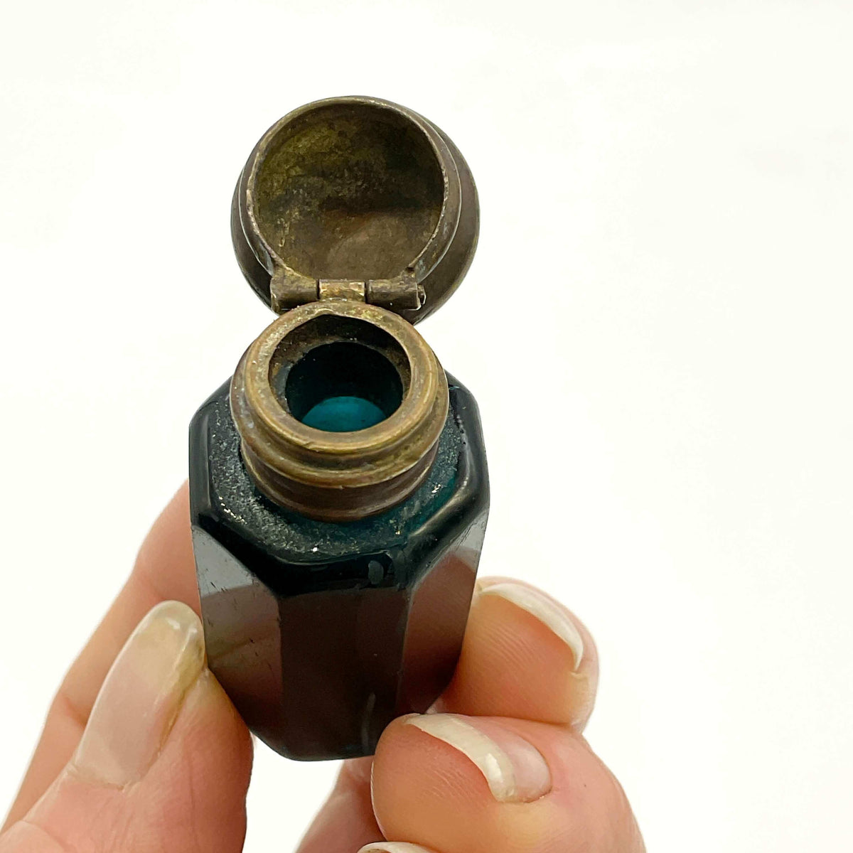 antique blue glass bottle with an open lid held by a hand on a white background